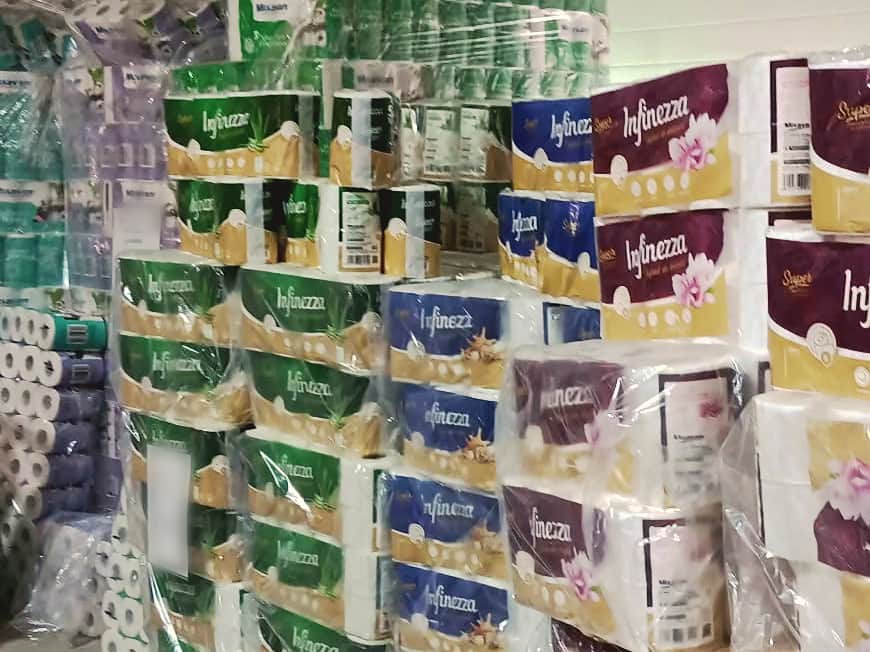 Paleți cu baxuri de hârtie igienică, stivuite în rânduri mov, verzi și albastre